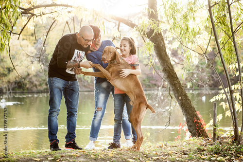 Family of father, mother and daughter on the riverside playing with their dog. Animal lovers
