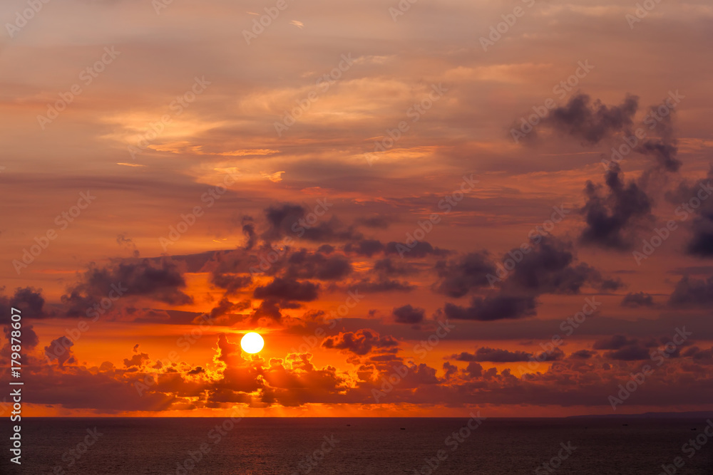 Bright colorful sun hides behind clouds of red color, goes beyond the horizon of the sea, the Indian Ocean. Amazing sunset from Uluwatu Temple, Bali, Indonesia.