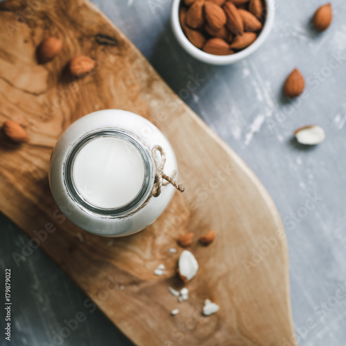 Top view of the almond milk in the glass bottle with almond nuts in the white bowl on the wooden decorative rustic cutting board.