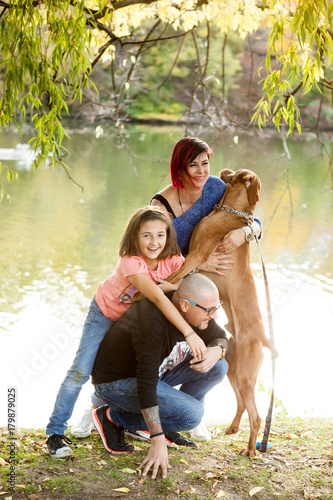 Happy gorgeous family of father, mother and daughter on the riverside playing with their dog. Animal lovers