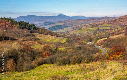 mountainous rural area in late autumn. trees with reddish foliage on green grassy hills. mountain ridge with high peak in the distance photo