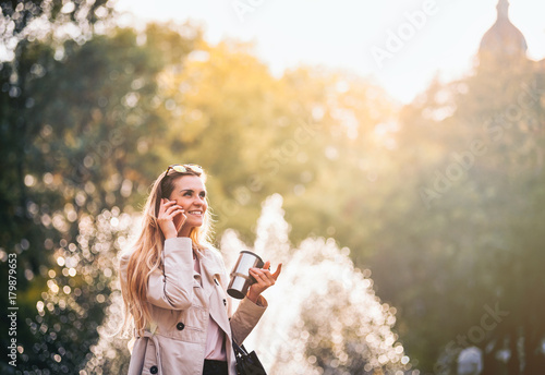 Modern woman in rush walking on street using smartphone outdoor