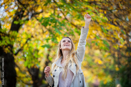 Cheerful woman in coat reaching hand to colorful autumn leaves