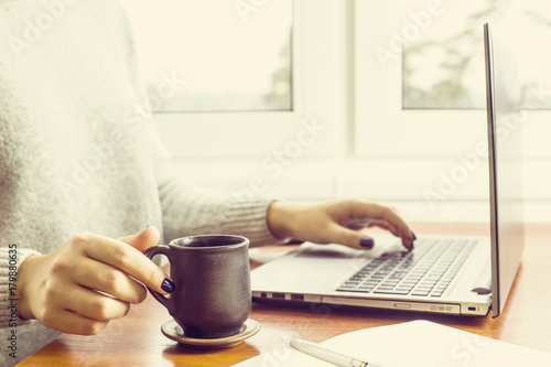 woman working at desk at home by the window with computer and cup of coffee