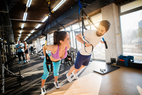 Young handsome fitness couple flirting while exercising with TRX in the gym.