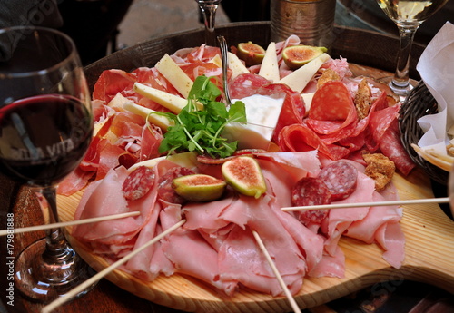 Rundes Holzbrett mit leckerem Schinken, Salami und Käse sowie Spießchen und einem Glas Rotwein im Vordergrund