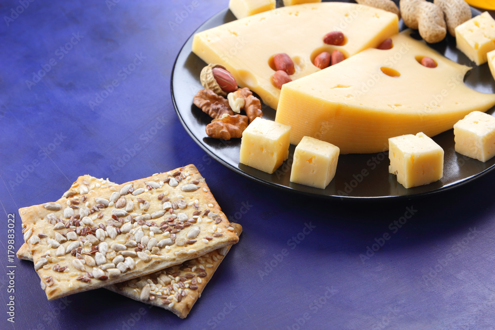 Hard cheese with holes on a black plate, cheese with peanuts, honey, biscuits, walnuts, cheese in minimalism style, cheese on dark blue background