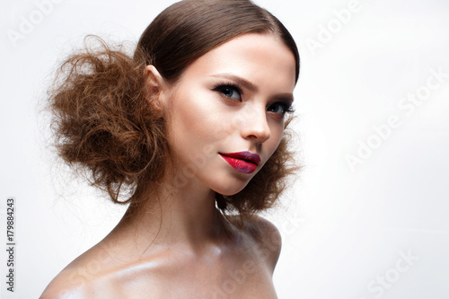 Young girl with creative bright makeup and shining skin. Beautiful model with a hairdo, arrows on eyes and red lips. Beauty of the face. Photo is taken in the studio. White isolated background. 