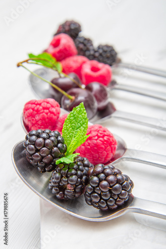 Fresh berries on steel spoons on white marble background 