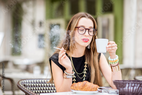 Young woman smoking a cigarette while having a breakfast outdoors at the typical french cafe terrace in France