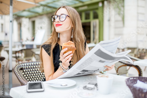 Photography Young woman reading newspaper during a breakfast with croissant sitting outdoors