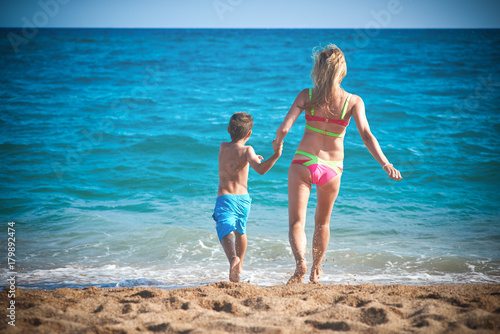 Caucasian mom and son running into the sea water. Back view. © Artem