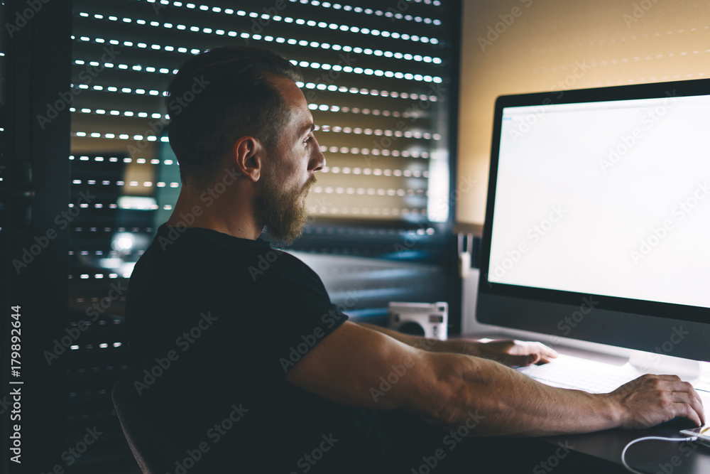 A bearded caucasian male is sitting behind the blank white monitor of the computer. Muscular hipster guy is looking at the blank display during working time. Empty space on the pc screen. A bearded caucasian male is sitting behind the blank white monitor of the computer. Muscular hipster guy is looking at the blank display during working time. Empty space on the pc screen.