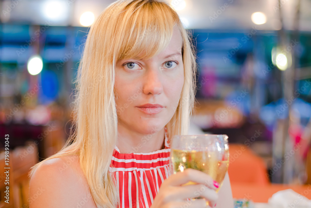 A beautiful young woman without makeup and blonde hair sitting in outdoor restaurant and holding a glass of wine. A beautiful young woman without makeup and blonde hair sitting in outdoor restaurant and holding a glass of wine.