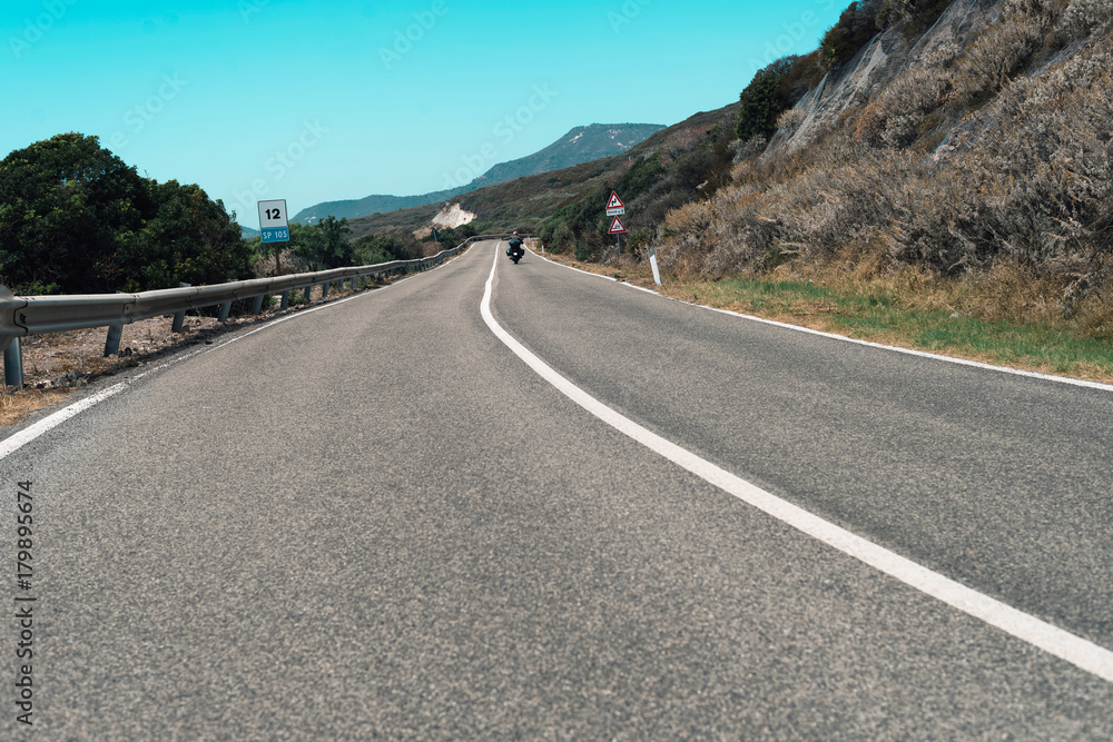 Motorcyclist driving on mountain road in summer. Sardinia. Italy.