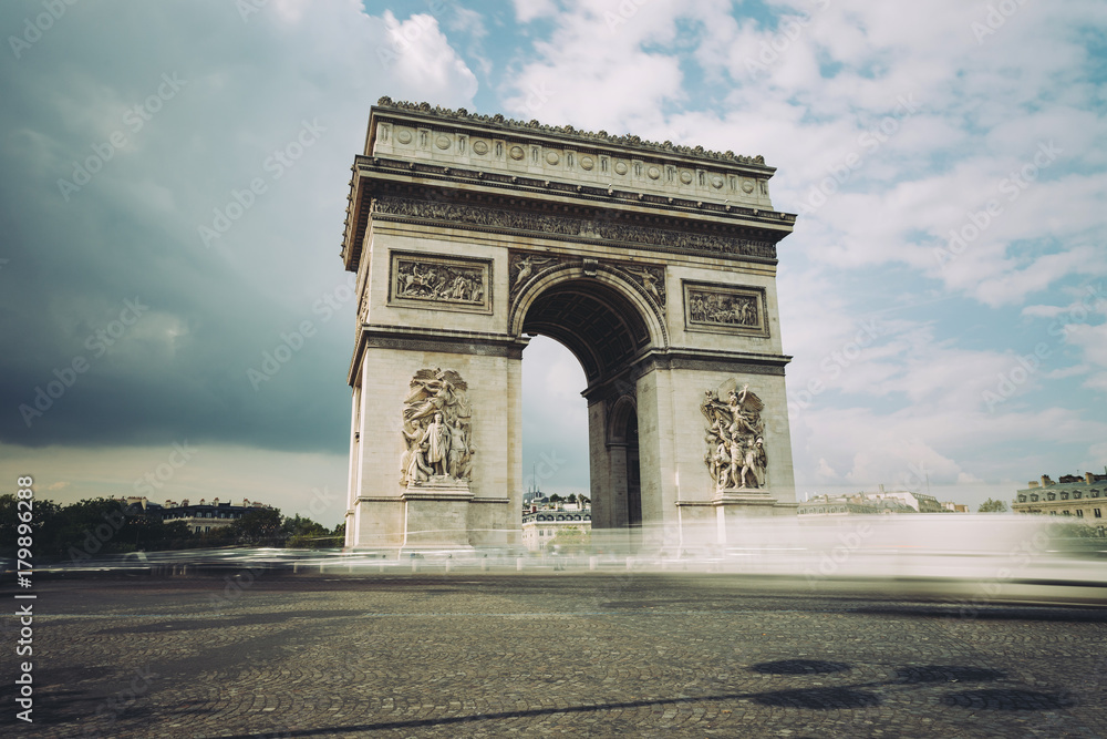 Famous Triumphal Arch, symbol of the glory and historical heritage. Iconic architectural landmark of Paris, France. Charles de Gaulle square. City traffic, tourism and travel concept. Long exposure.