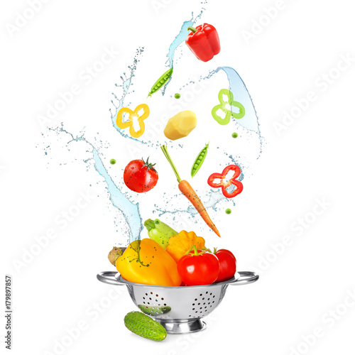 Fototapeta Naklejka Na Ścianę i Meble -  Different vegetables, water splashes and colander on white background