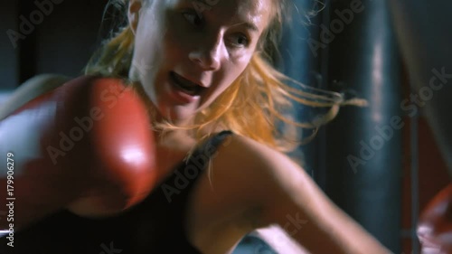 A girl is a boxer. The girl is training in the boxing hall. The girl is beating a punching bag.