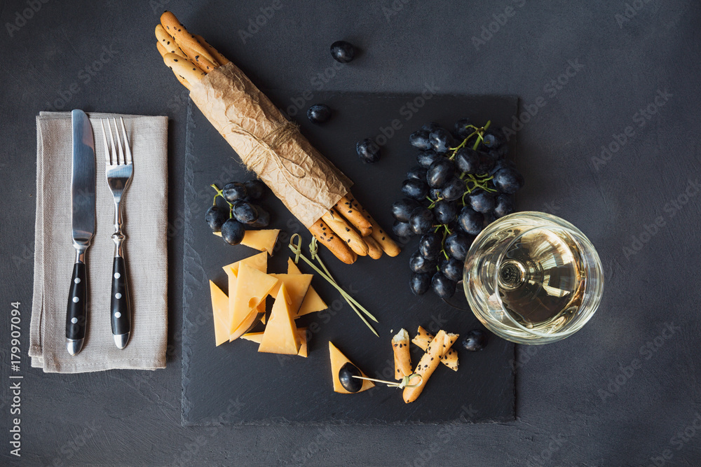 Cheese plate served with crackers, grapes and glass of white wine on dark background. - obrazy, fototapety, plakaty 
