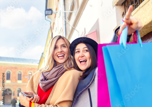 Two smiling young woman with shopping bag in the city on sunny autumn day.