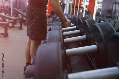 The hand of a strong man takes a heavy dumbbell in the gym.