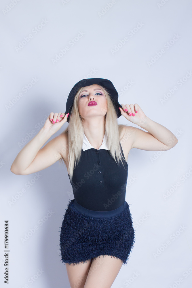 Portrait of a beautiful young woman who tries on a black hat. Girl posing against white background in studio. Portrait of a beautiful young woman who tries on a black hat. Girl posing against white background in studio.