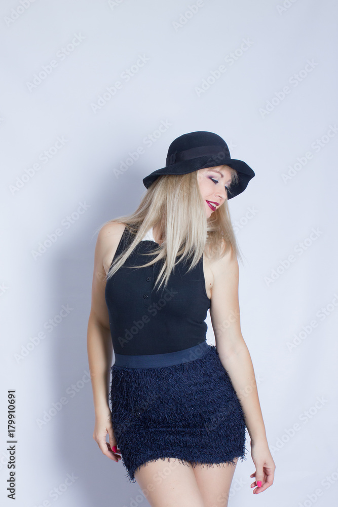Portrait of a beautiful young woman who tries on a black hat. Girl posing against white background in studio. Portrait of a beautiful young woman who tries on a black hat. Girl posing against white background in studio.