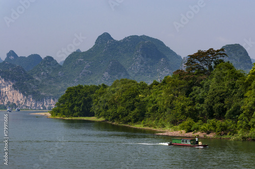 Yangshuo, China - August 1, 2010: Small boal in the Li River with the tall limestone peaks in the background near Yangshuo in China, Asia.
