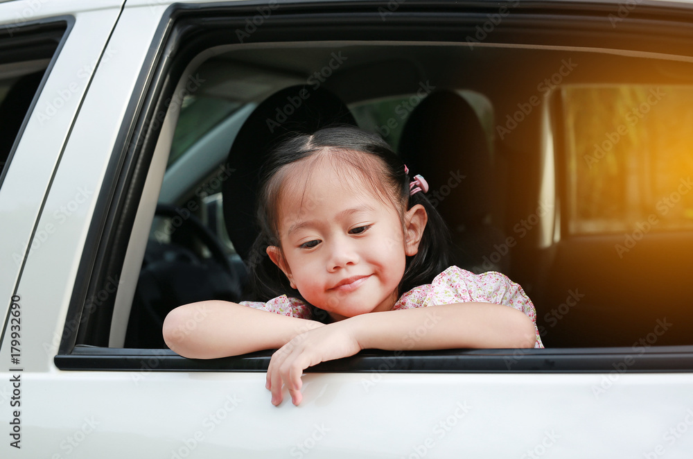 Happy little asian child looking out from the window of the car.