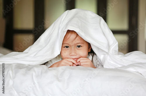 Cute little asian girl playing under a white blanket on the bed at home.