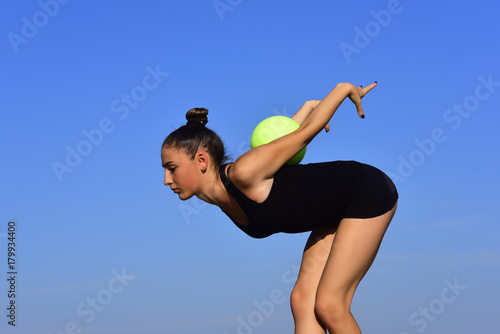 Woman gymnast with green ball on blue sky background