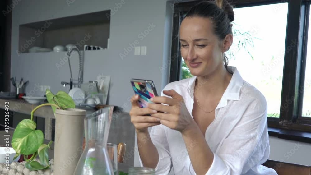 Young, pretty woman texting on smartphone sitting by table in kitchen at home
Young, pretty woman texting on smartphone sitting by table in kitchen at home
