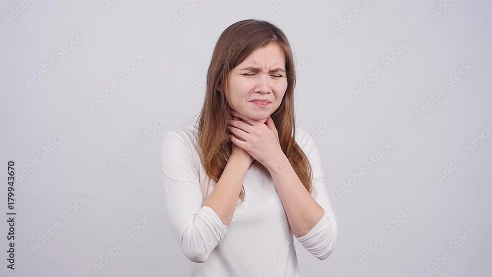 A young woman has a sore throat on a gray background A young woman has a sore throat on a gray background