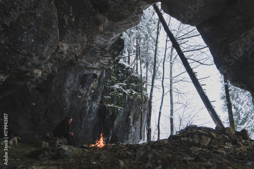 a man with a beard looks at the fire near the cave photo