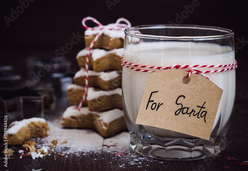 Cookies for Santa with glass of milk with tag for Santa and christmas tree