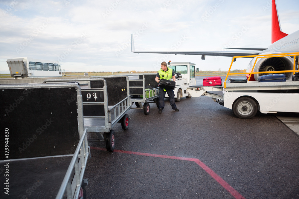 Worker Placing Luggage In Trailer On Runway