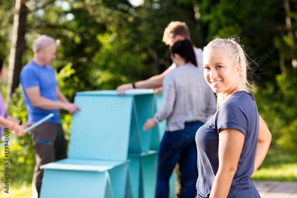 Fototapeta premium Smiling Young Woman While Coworkers Making Pyramid Of Planks
