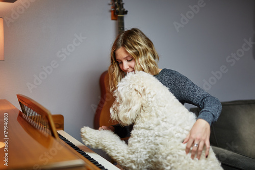 young blond woman playing piano with goldendoodle