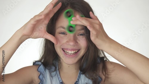 Beautiful cheerful teen girl spinning a green fidget spinner on her forehead on white background stock footage video photo