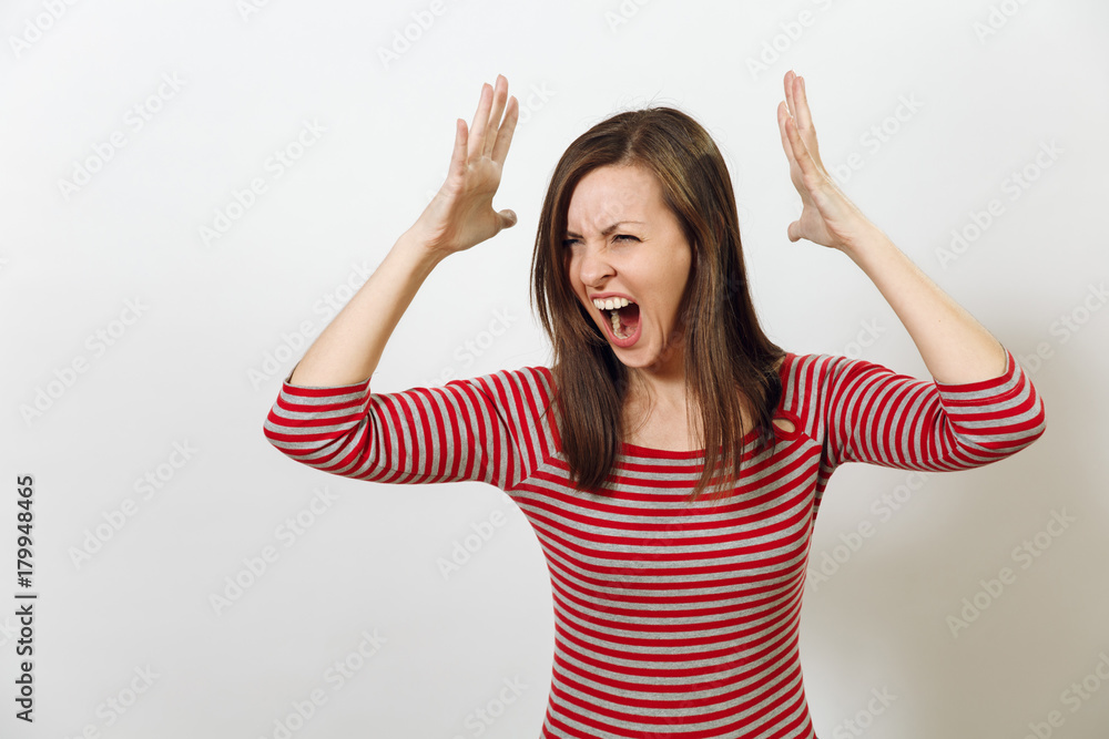 Fototapeta premium Pretty European young angry brown-haired woman with healthy clean skin, dressed in casual red and grey clothes, screaming, swearing and waving her arms, on a white background. Emotions concept.