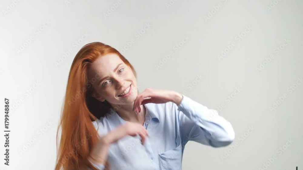 Portrait of beautiful cheerful redhead girl with flying curly hair smiling laughing looking at camera over white background. Slow motion. Portrait of beautiful cheerful redhead girl with flying curly hair smiling laughing looking at camera over white background. Slow motion.