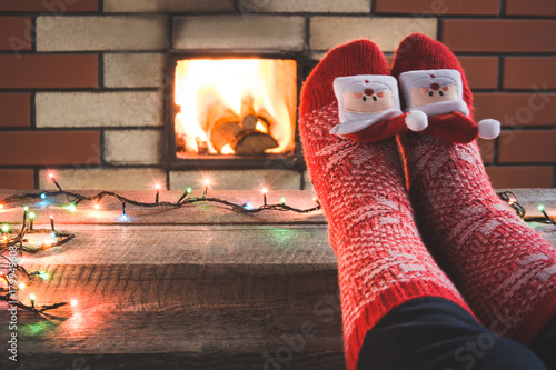 Slika na platnu Feet in woollen red christmas socks by the fireplace