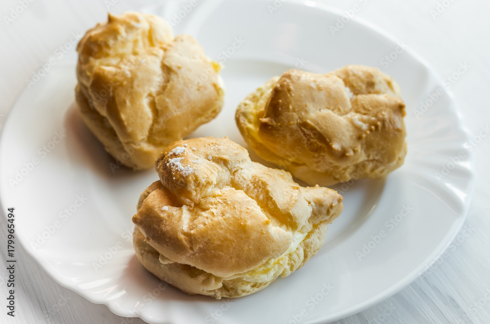 Homemade baked cream puffs on the white plate on light wooden table Homemade baked cream puffs on the white plate on light wooden table