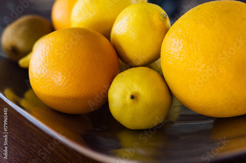 Orange lemon grapefruit in metal dish on the wooden table daylight