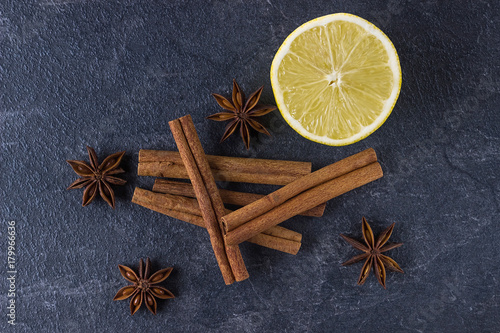 Cinnamon sticks, lemon and anise stars on a black stone background.