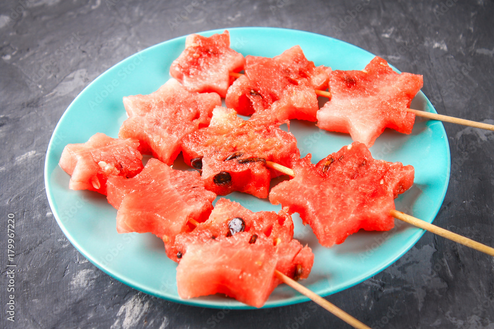 Watermelon in the form of stars on skewers lies on a plate. The blue dish is like a rocket in space. Top view. Watermelon in the form of stars on skewers lies on a plate. The blue dish is like a rocket in space. Top view.