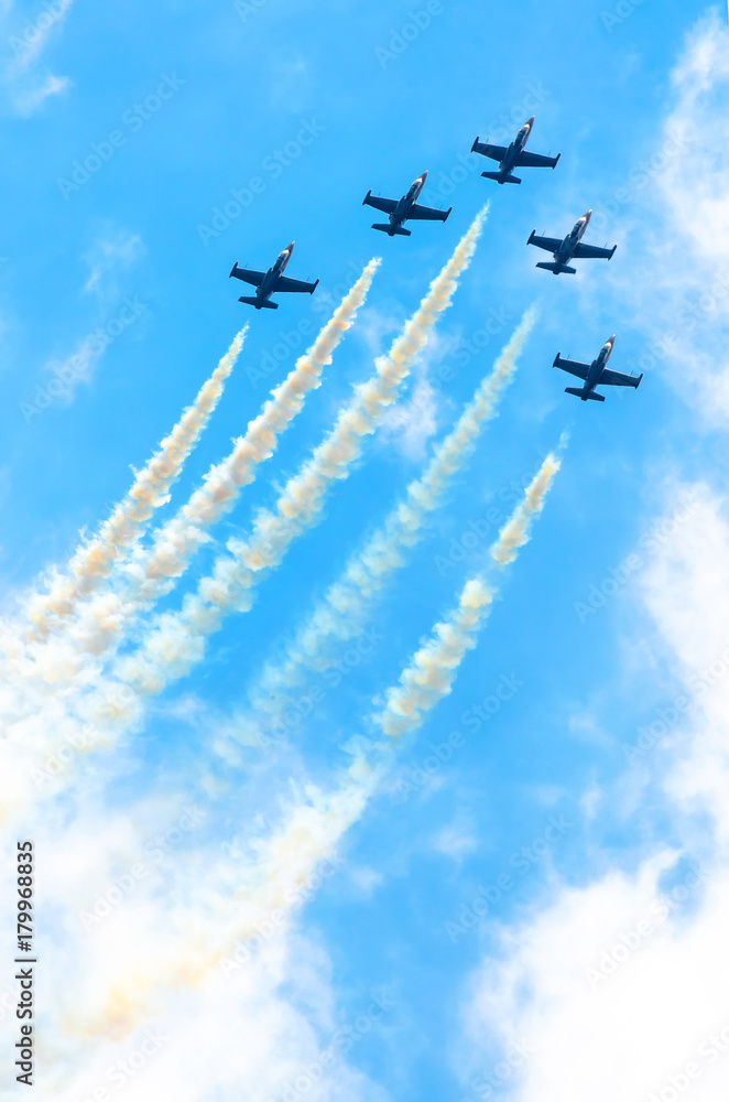 Group of fighter planes fly up with a smoke track against a blue sky with clouds. Group of fighter planes fly up with a smoke track against a blue sky with clouds.