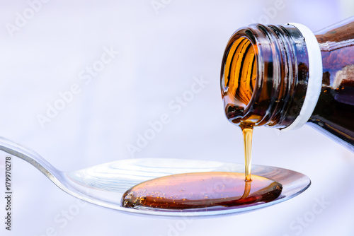 Hand pouring medication or antipyretic syrup from bottle to spoon. healthcare, people and medicine concept.