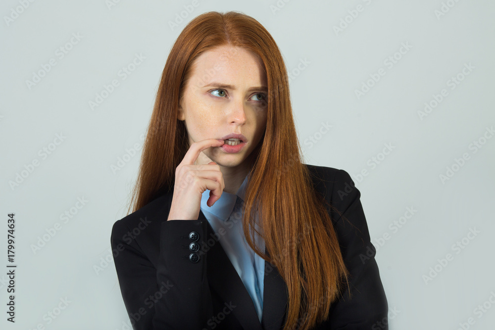 beautiful young girl with red hair in a black jacket reflects with a strained face on a light background beautiful young girl with red hair in a black jacket reflects with a strained face on a light background
