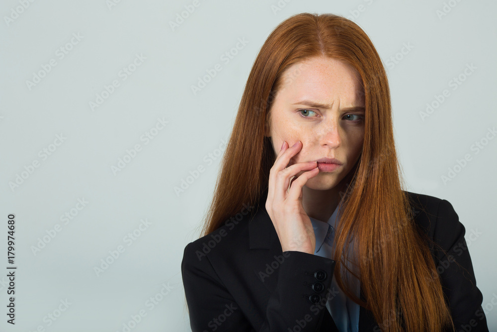 beautiful young girl with red hair in a black jacket reflects with a strained face on a light background beautiful young girl with red hair in a black jacket reflects with a strained face on a light background